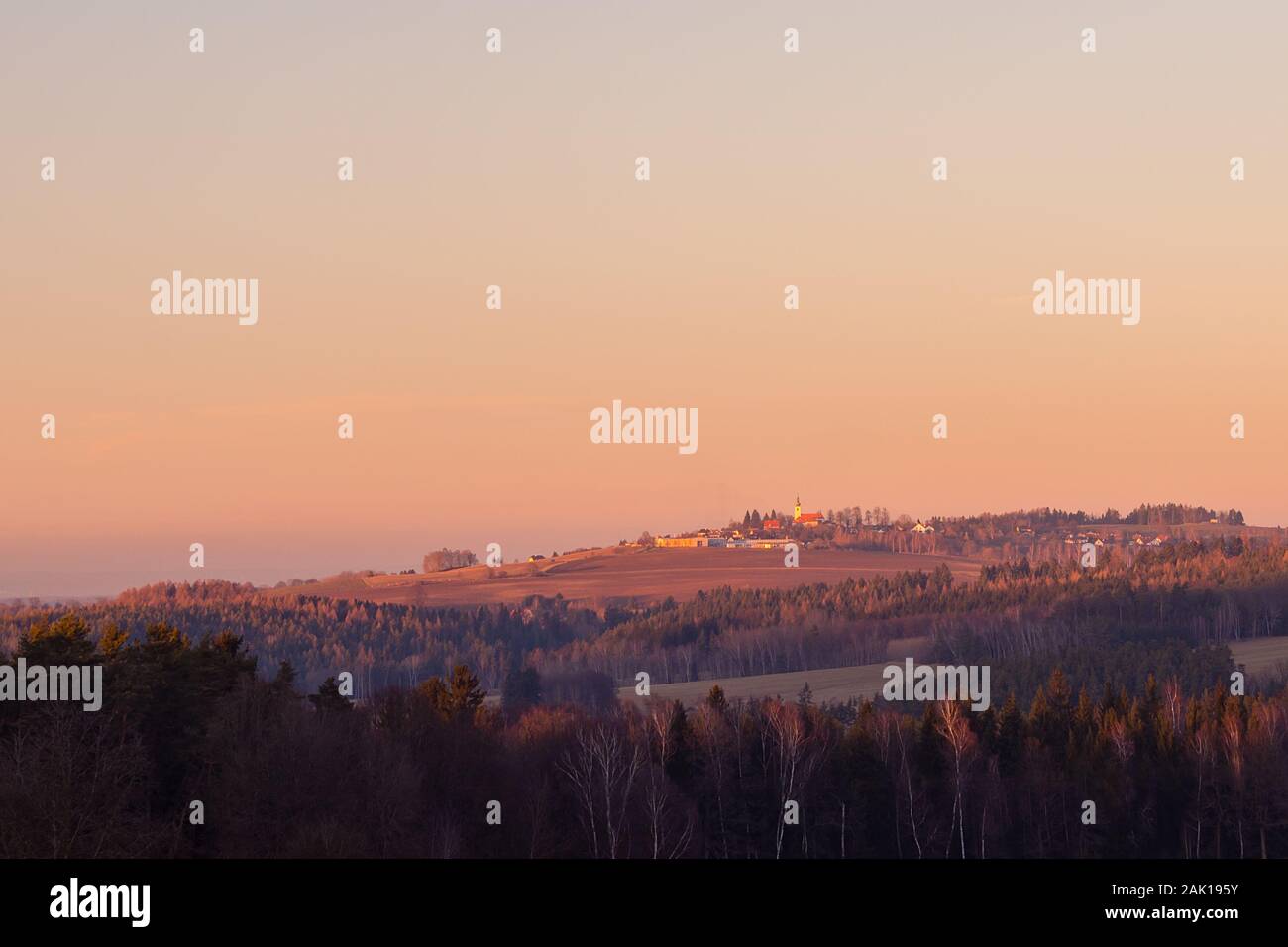 tramonto sul paesaggio rurale con villaggio - nella foresta in primo piano, all'orizzonte sulla collina chiesa e diversi edifici, colore arancione cielo Foto Stock