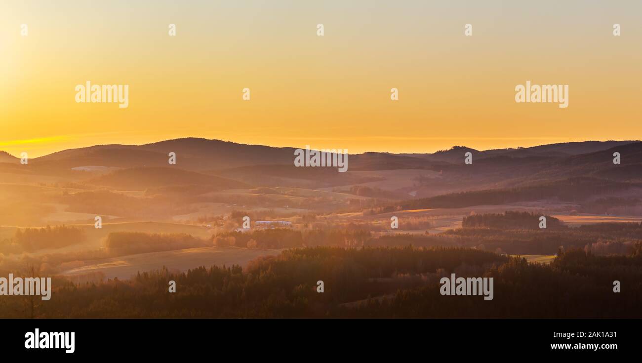 alba in montagna - paesaggio collinare con prati e foreste in una foschia, in un cielo giallo e arancione Foto Stock