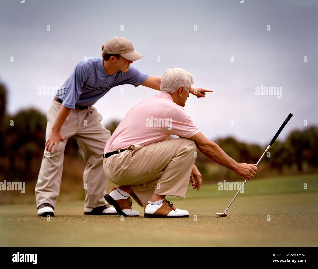 Giovane uomo che consiglia l'uomo anziano sul suo putt seguente durante il gioco del golf. Foto Stock