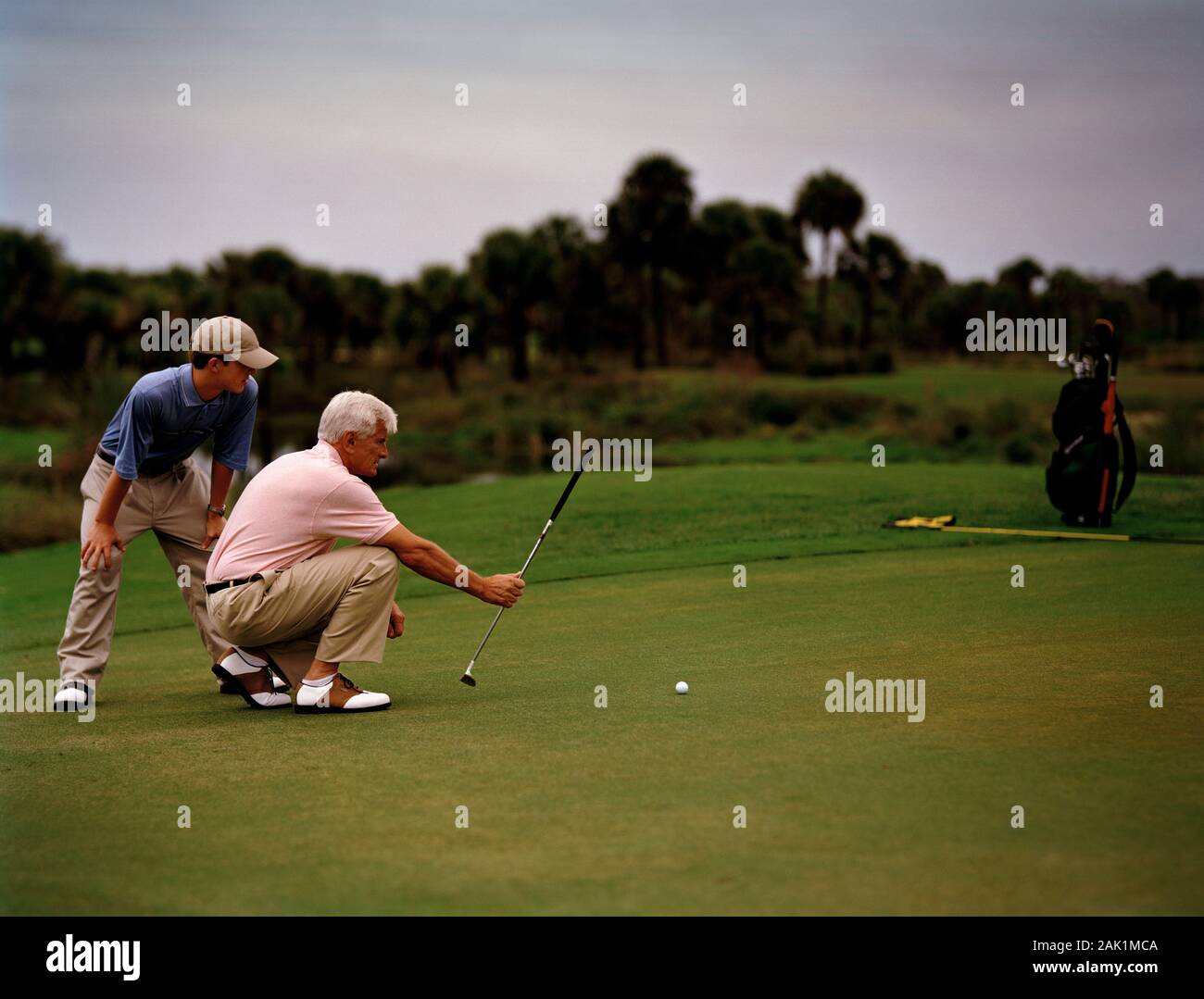 Giovane uomo che consiglia l'uomo anziano sul suo putt seguente durante il gioco del golf. Foto Stock