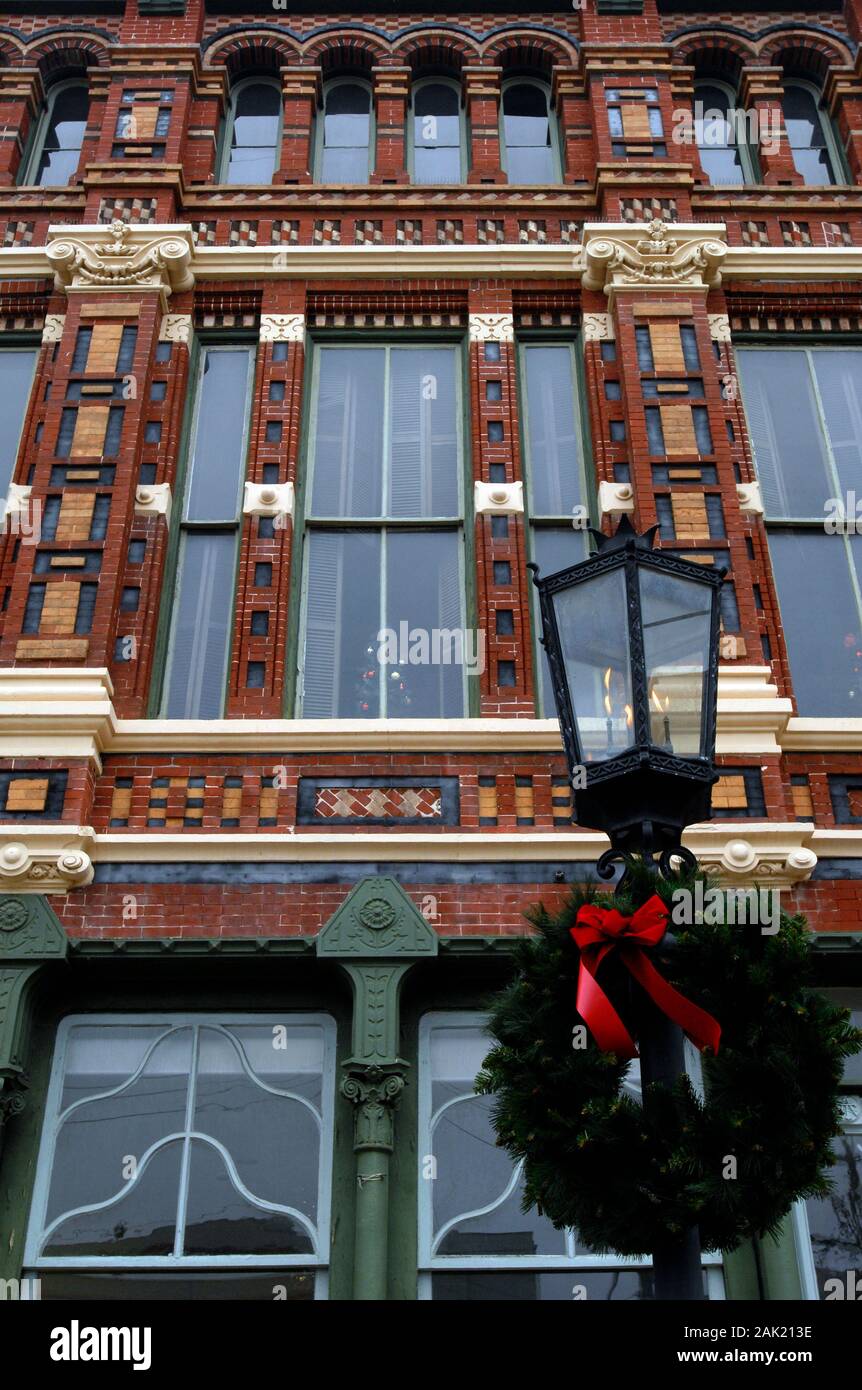 Un giuramento di Natale decora una lampada a gas di fronte ad un edificio commerciale vittoriano decorato nel quartiere storico Strand a Galveston, Texas. Foto Stock