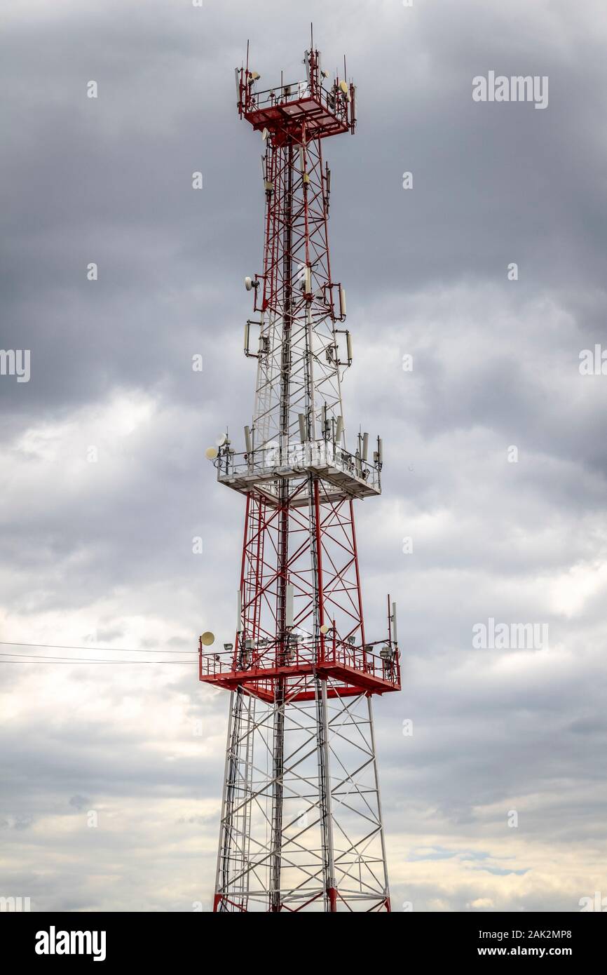 Un grande rosso e bianco torre cellulare contro il grigio di un cielo nuvoloso. Foto Stock