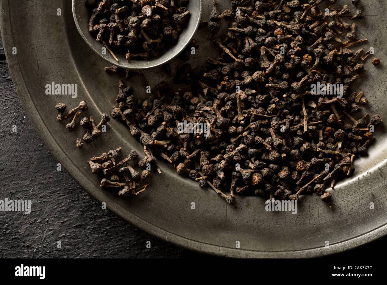 Cumulo di materie, essiccato cannella dei boccioli spice sulla piastra di metallo con metallo scoop su rustico tavolo nero lo sfondo con il fuoco selettivo Foto Stock