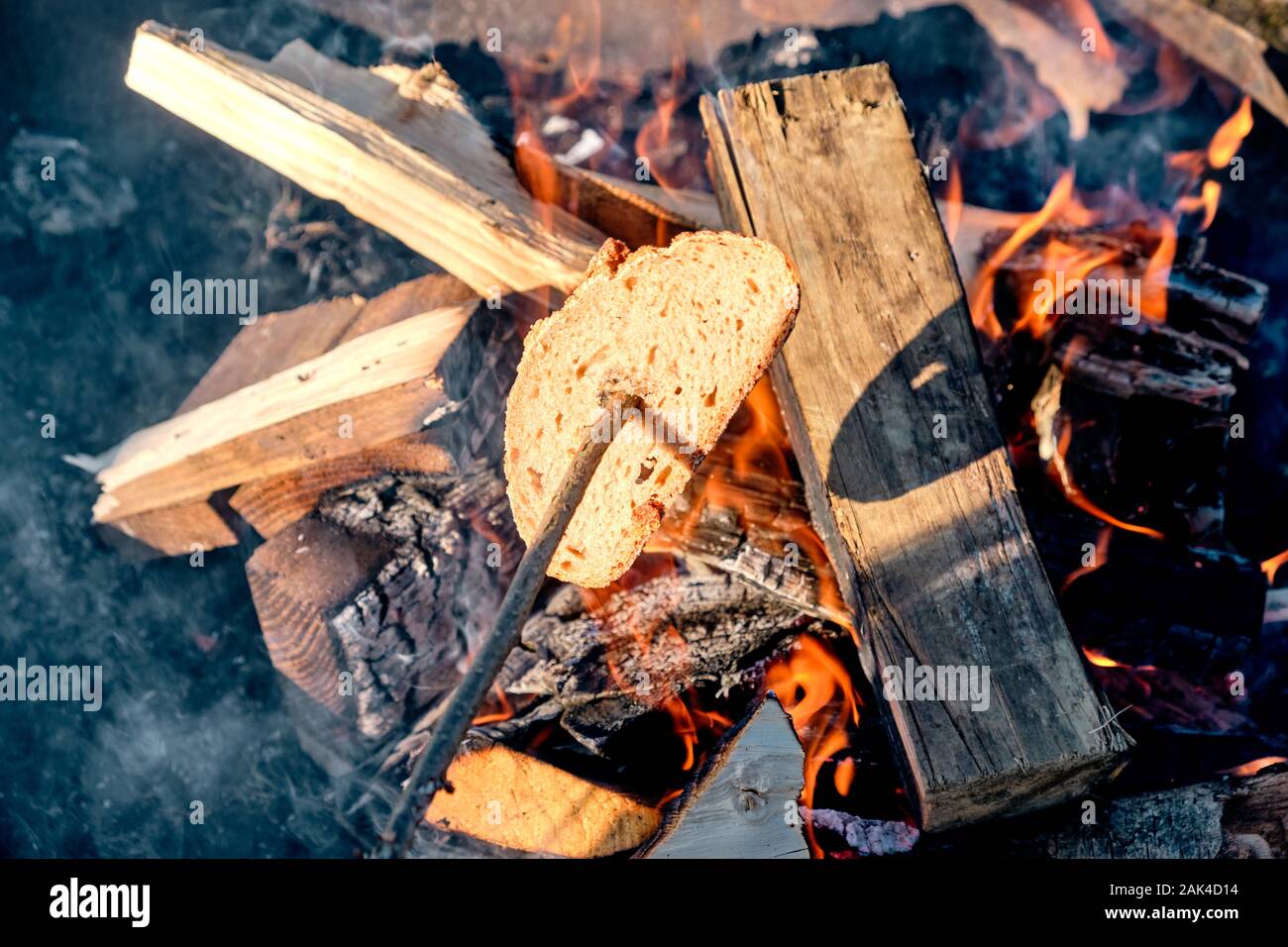 Tostare un pezzo di pane su un bastone di legno al di sopra di un falò con fiamme di colore arancione e uno splendido bagliore a caldo in un firebowl. Visto in Baviera, Germania nel Gennaio Foto Stock