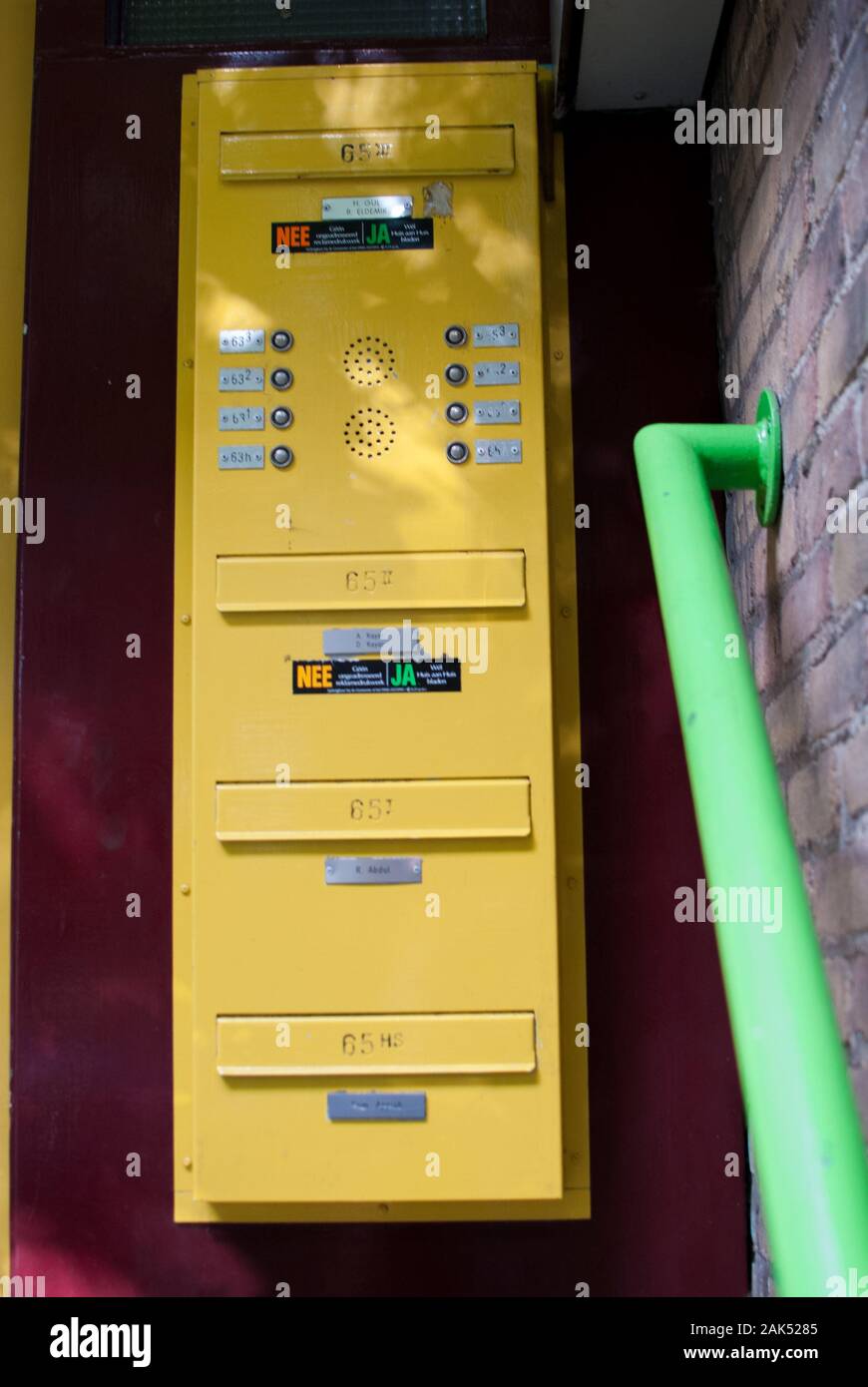 Cassetta postale di giallo e il campanello e corrimano verde con una parete di borgogna sul retro Foto Stock