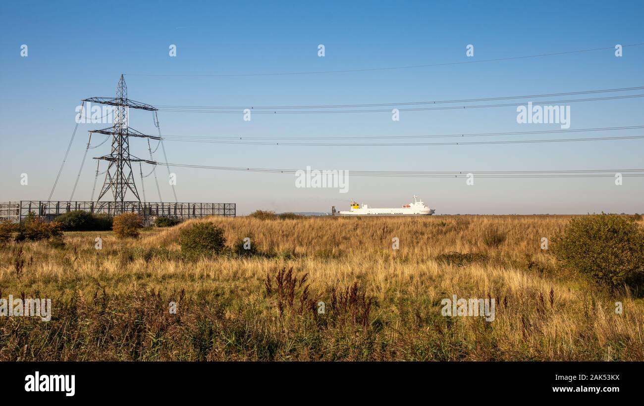 Gravesend, England, Regno Unito - 21 Settembre 2010: una nave cargo vele sull'estuario del Tamigi accanto a terra desolata e linee di alimentazione a Gravesend. Foto Stock