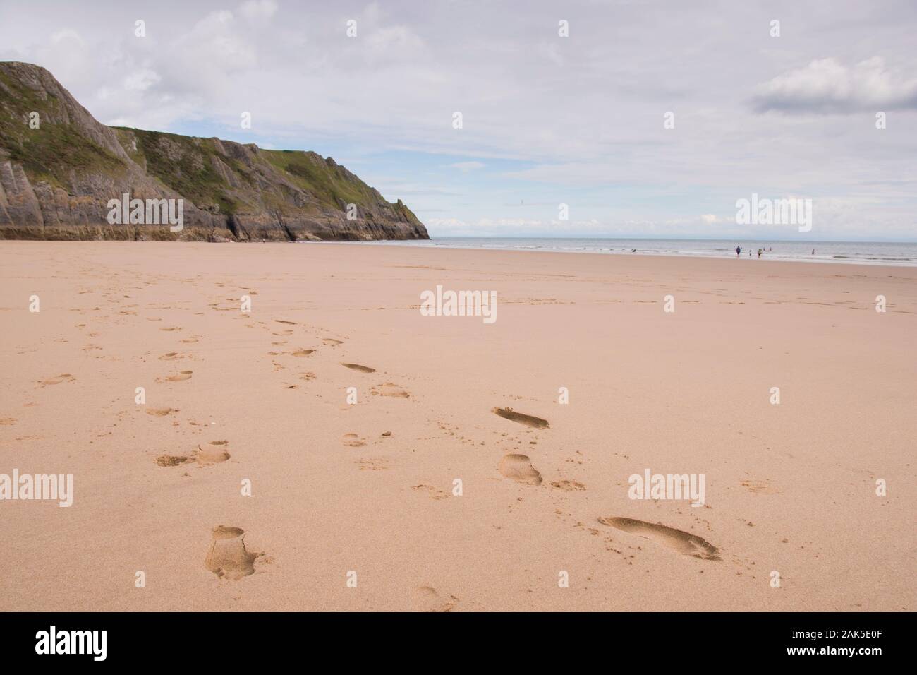 Un ampio tratto di spiaggia sabbiosa con impronte che conducono verso il lontano scogliere a tre cime Bay sulla Penisola di Gower, Galles Foto Stock