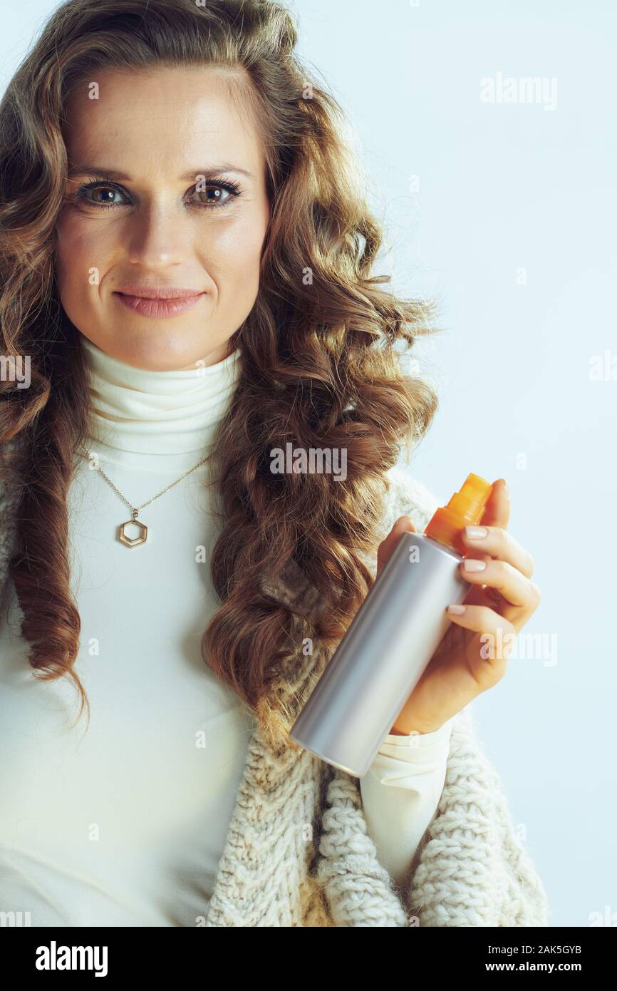 Elegante casalinga con lunghi capelli ondulati in maglione collo e cardigan con cura dei capelli prodotto isolato sulla luce invernale sfondo blu. Foto Stock