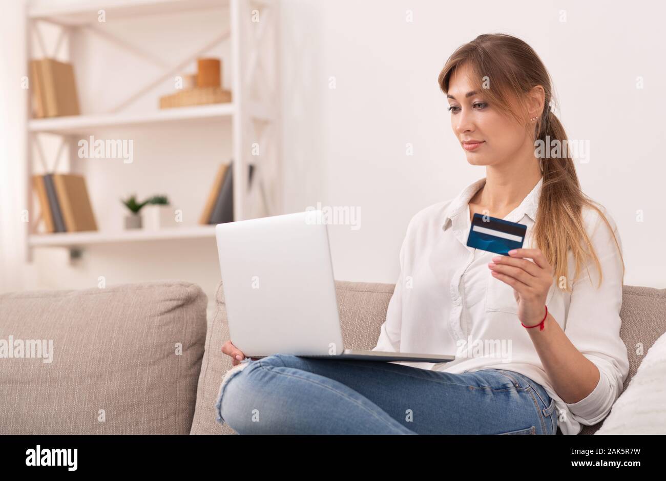 Shopping online. Donna con notebook Azienda Carta di Credito Acquisto e acquistare su Internet seduti sul divano di casa. Foto Stock