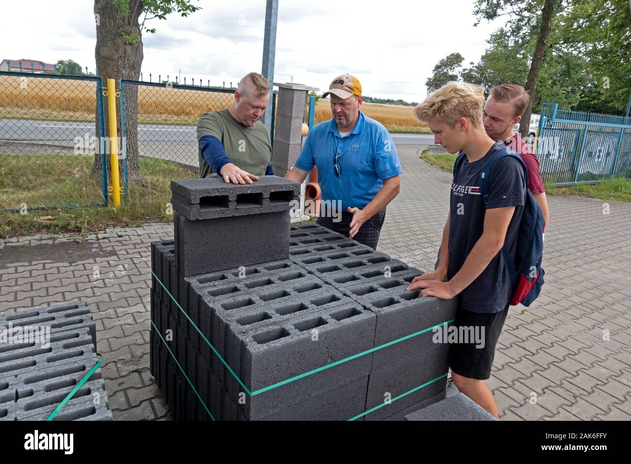 Due papà ciascuno con i propri figli adolescenti cercando di mattoni e la realizzazione di un progetto di costruzione di un caminetto all'aperto. Rzeczyca Polonia centrale Europa Foto Stock