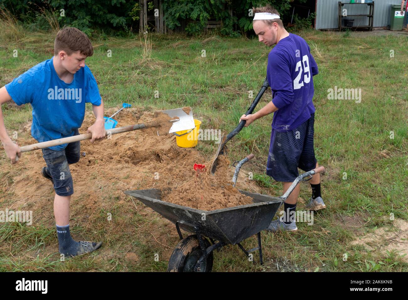 Cugini adolescenti lavorando insieme mettere sabbia in carriola per aiutare a rendere il cemento per un caminetto all'aperto. Zawady Gmina Polonia Rzeczyca Foto Stock