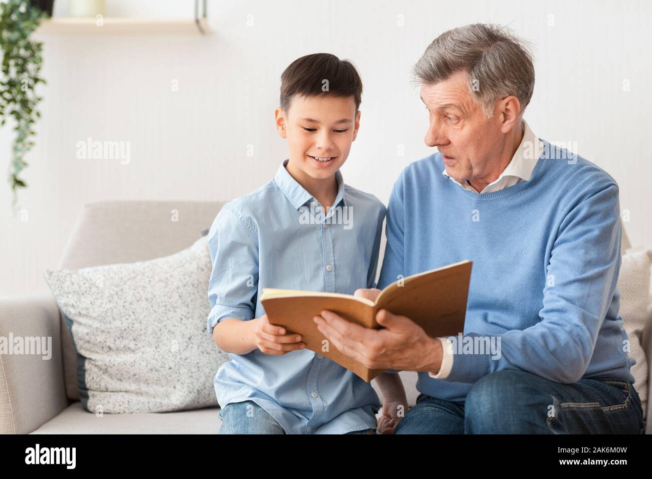 Anziani nonno e nipote ragazzo lettura libro seduti insieme sul divano di casa. Week-end in famiglia. Messa a fuoco selettiva Foto Stock