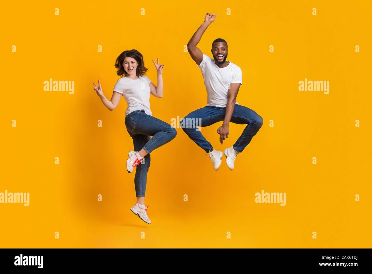 Gioiosa ragazzo e ragazza jumping in funny pose, interracial matura per divertirsi insieme su sfondo giallo in studio, spazio libero Foto Stock