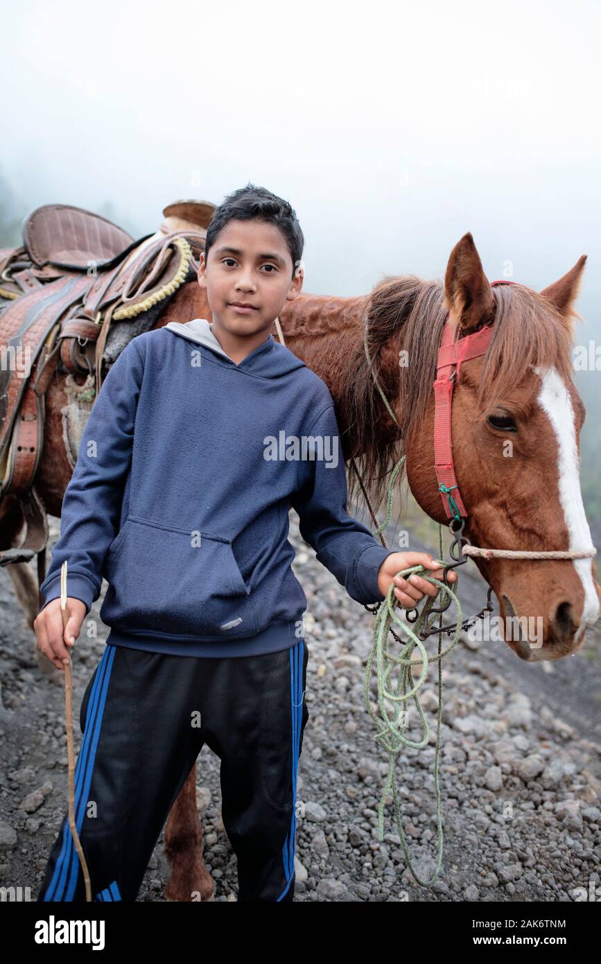 Ritratto di 11-anno-vecchio ragazzo di indigeni. Alcuni locali offrono passeggiate a cavallo per i turisti sul terreno vulcanico ed escursione al vulcano Pacaya, Guatemala Foto Stock