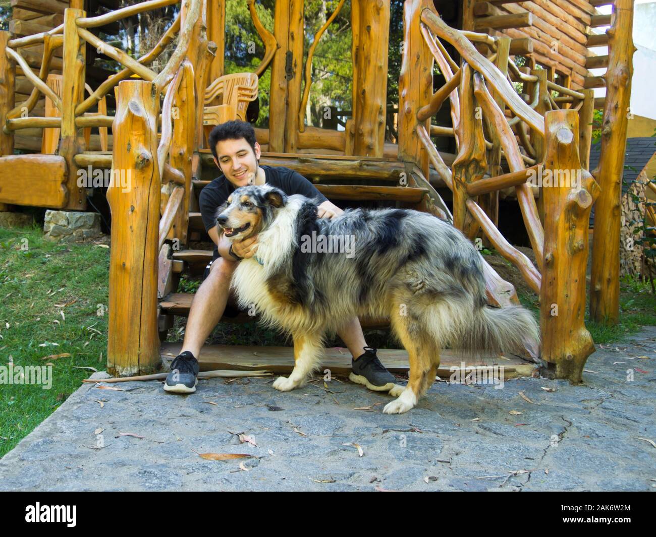 Giovane uomo caucasico petting a tre gambe ruvida Collie cane. L'uomo è seduto su una scala di legno. Amore Animali concetto. Foto Stock