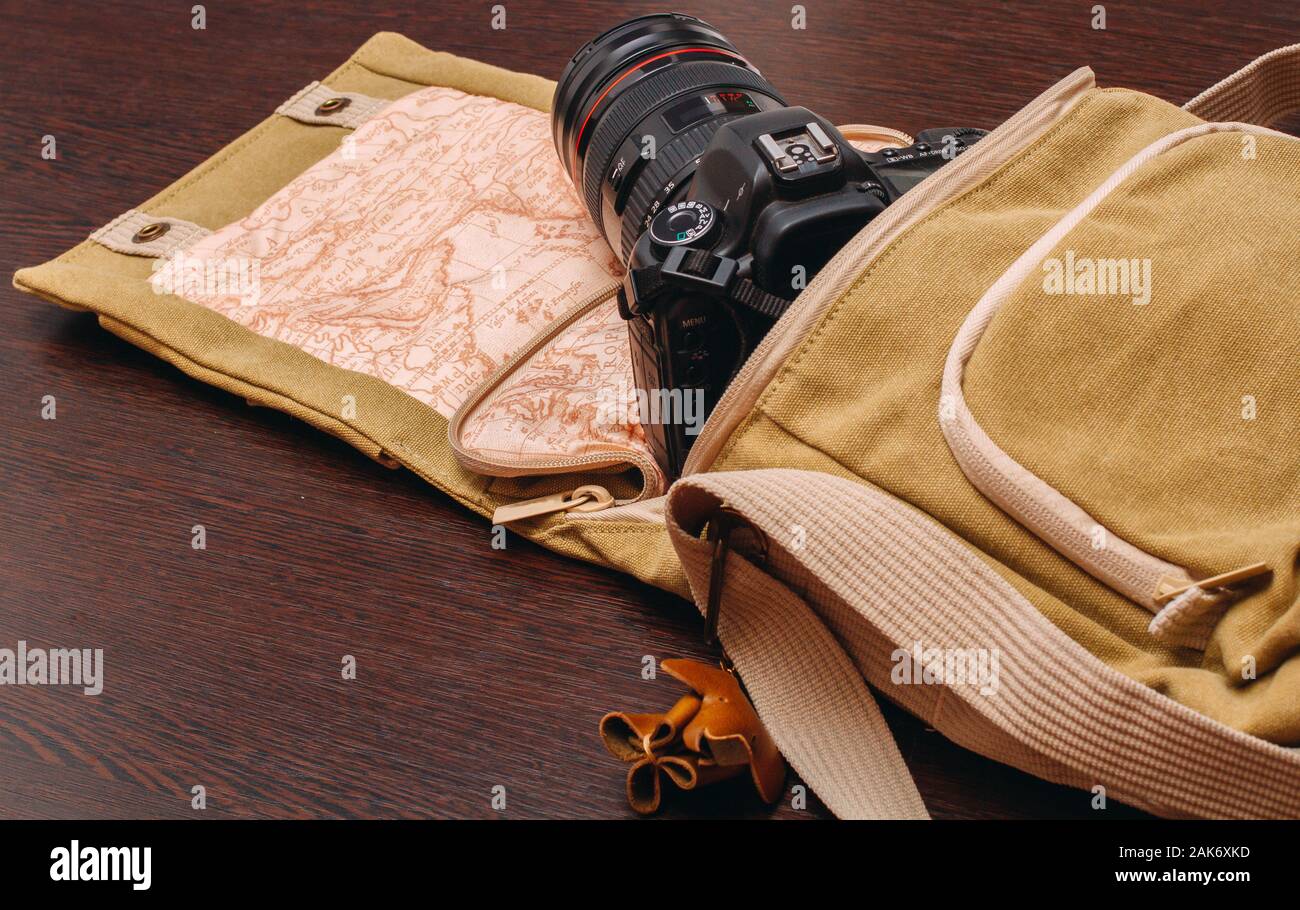 La fotocamera è in una borsa da viaggio che si estende su una superficie di legno Foto Stock