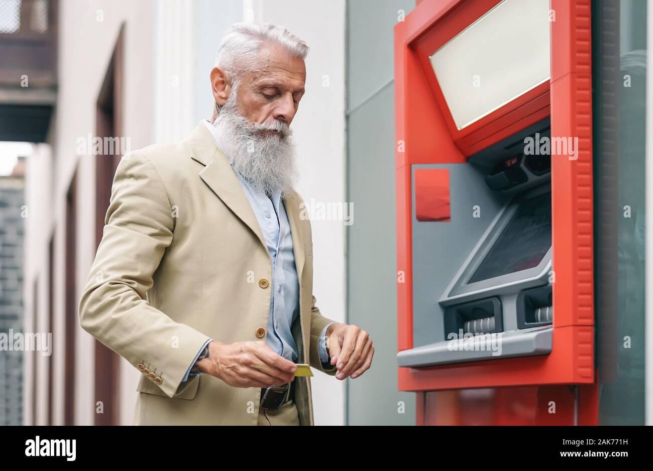 Uomo senior di ritirare i soldi dalla banca bancomat con la carta di debito - barbuto hipster maschio maturo di fare il pagamento con carta di credito in ATM Foto Stock