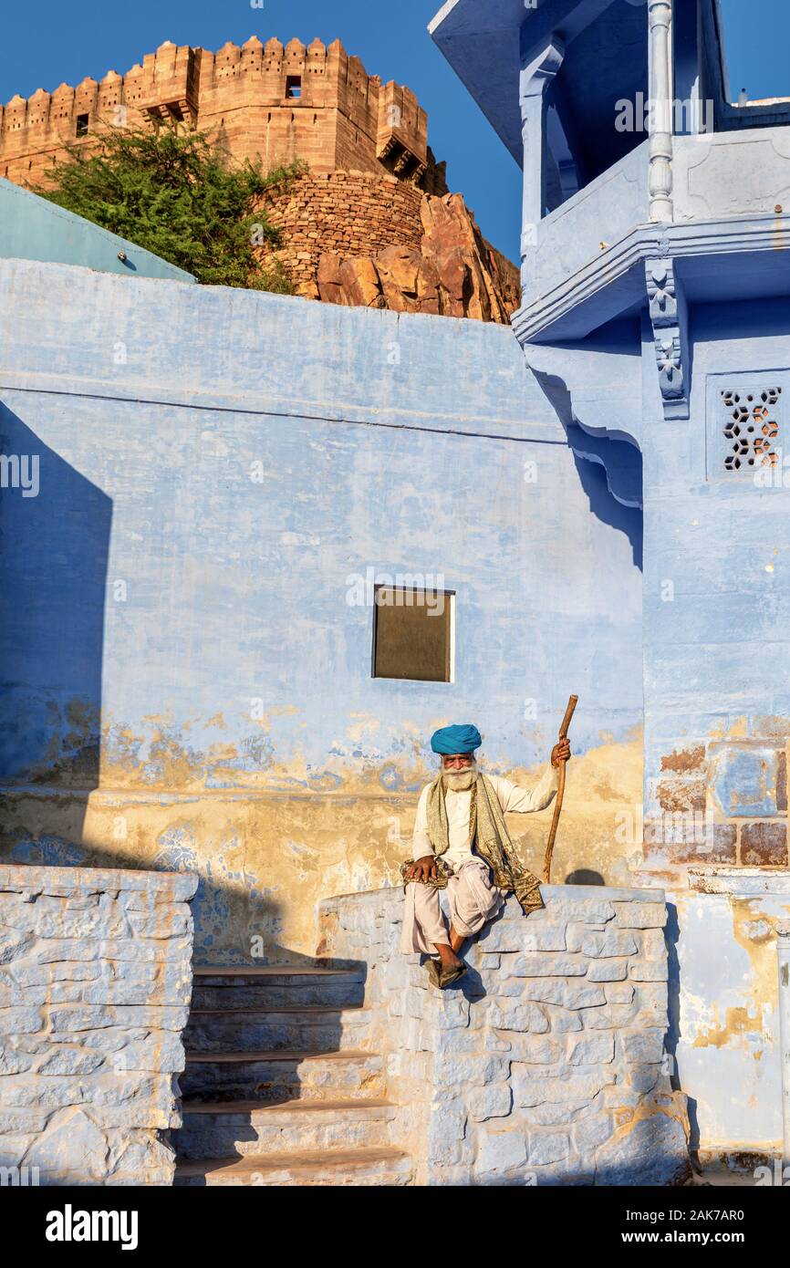 Un uomo anziano in appoggio nelle città blu di Jodhpur con il Forte Mehrangarh in background, Jodhpur, Rajasthan, India Foto Stock