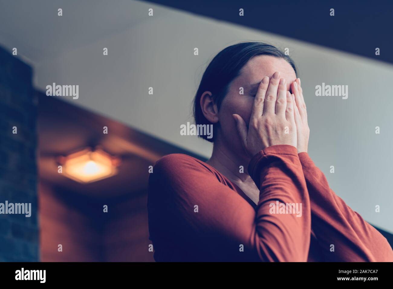 Premuto donna che ricopre la faccia con le mani e a piangere in appartamento loft, il fuoco selettivo Foto Stock