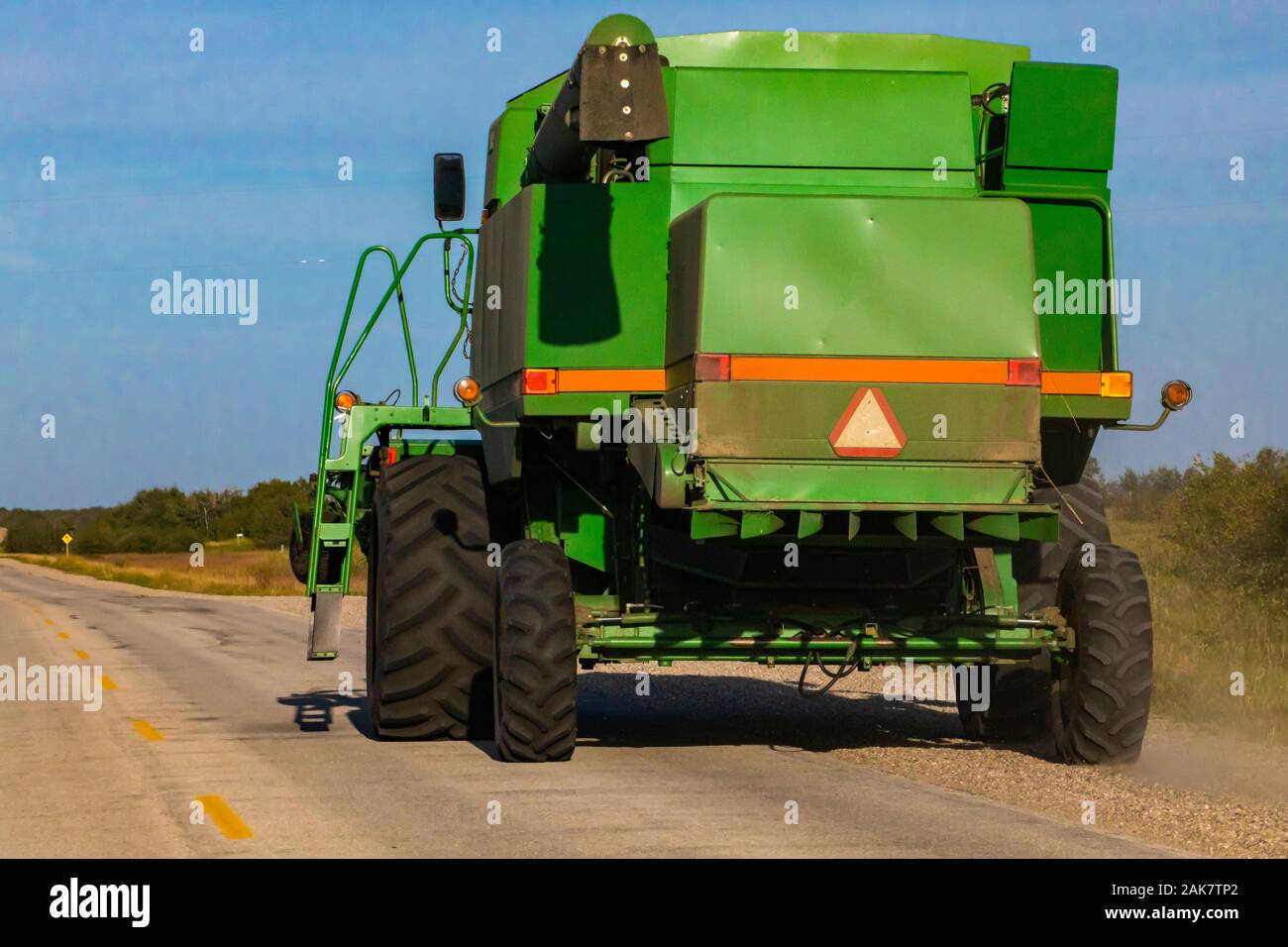 Un ampio e verde macchina mietitrebbiatrice è visto da dietro, parcheggiato su una strada di campagna. Il simbolo di attenzione e di nastro ad alta visibilità avvisa di veicolo lento Foto Stock