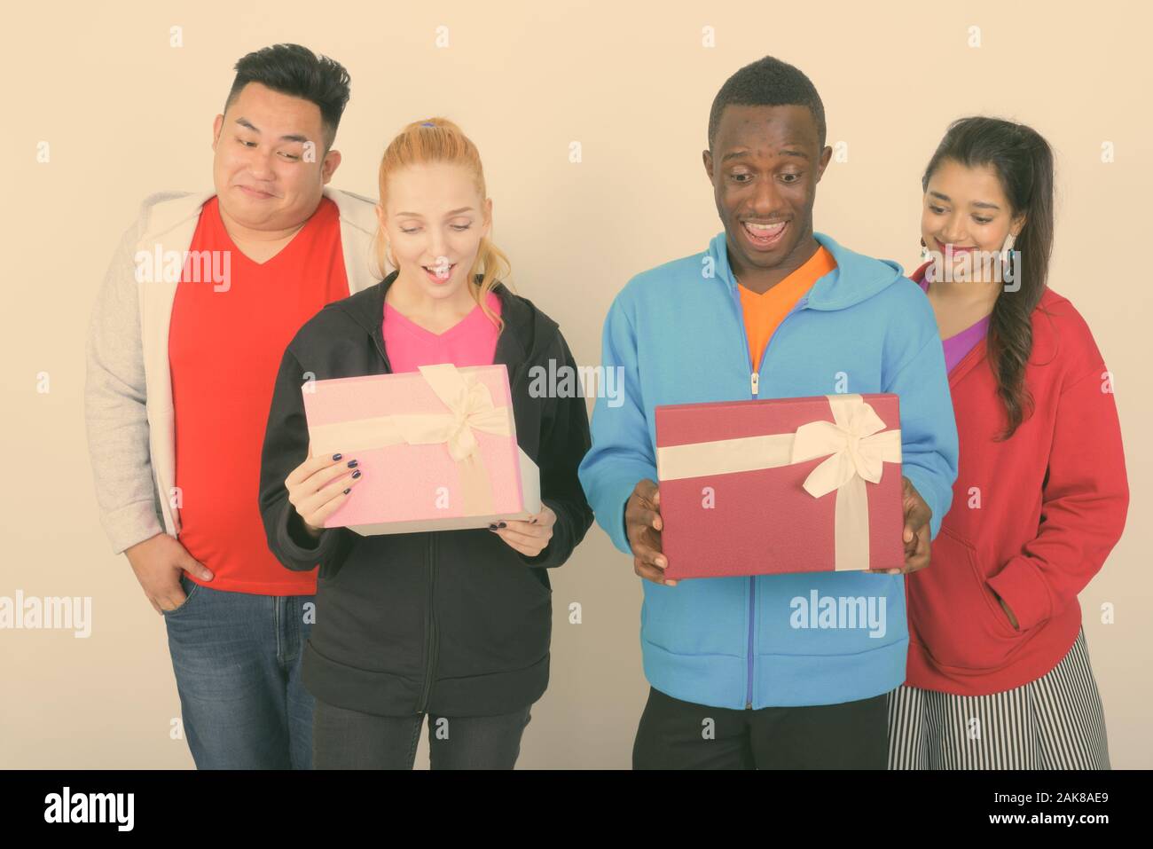 Studio shot di felice variegato gruppo di multi etnico sorridente amici durante l'apertura di confezioni regalo e guardando sorpreso insieme Foto Stock