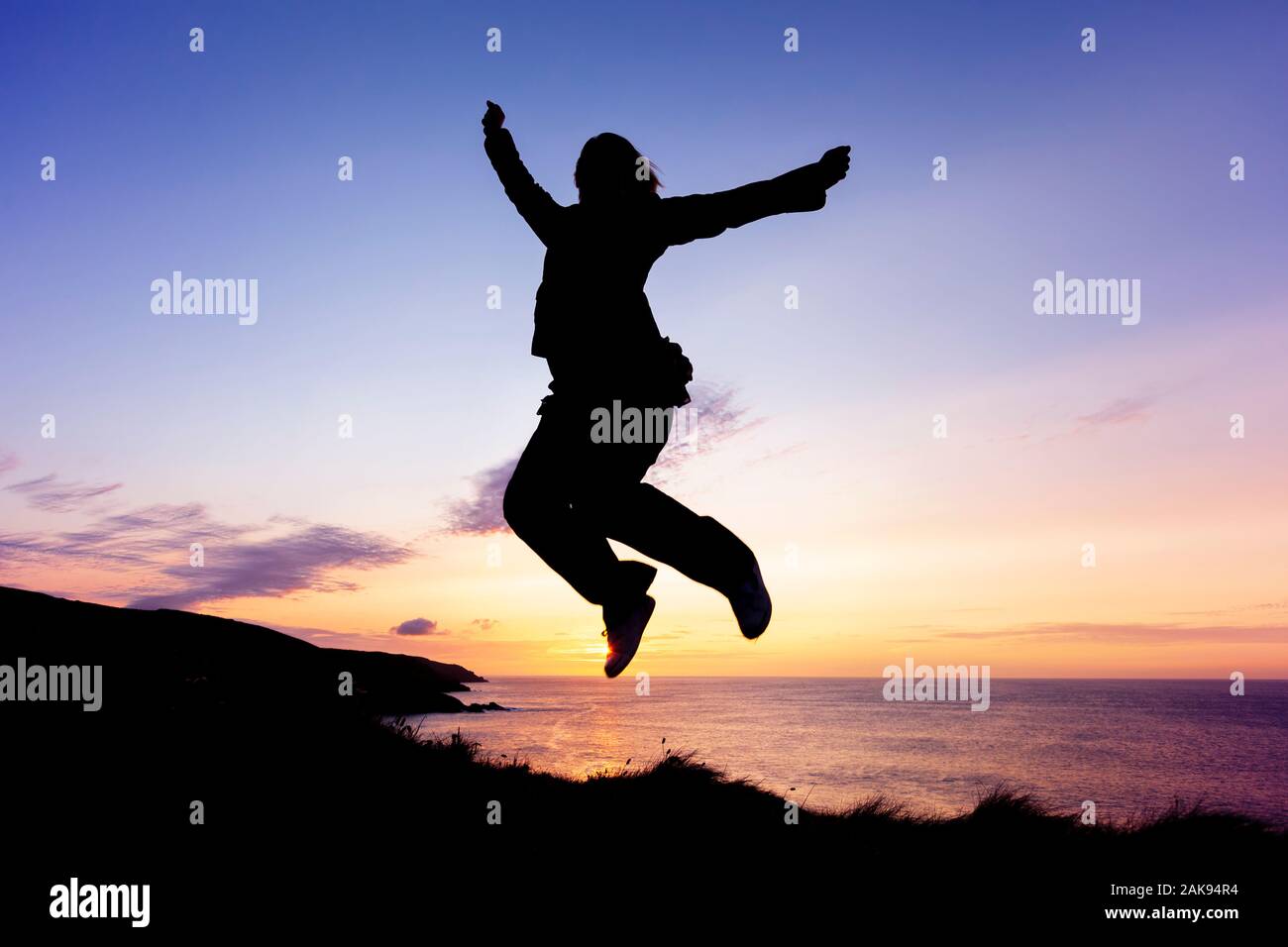 Silhouette di donna salti di gioia sul clifftops costiero al tramonto Foto Stock