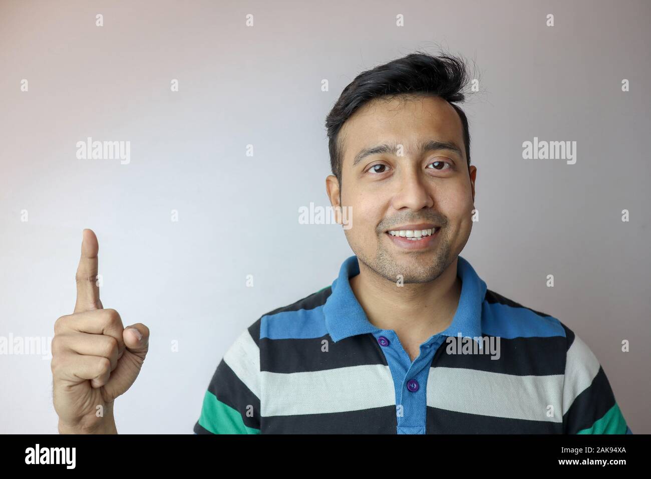 Un giovane uomo indiano fiducioso e sorridente che indica un simbolo isolato in uno sfondo bianco con copia spazio per il testo. Foto Stock