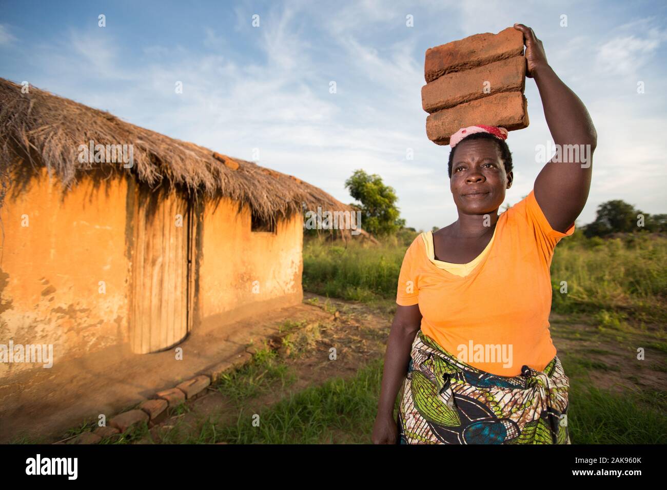Una donna malawiana porta un headload di mattoni per aiutare a costruire una banca del seme che aumenterà il suo villaggio di sicurezza alimentare. Foto Stock