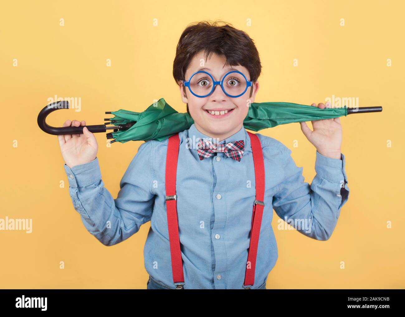 Bambino con ombrello verde su sfondo giallo Foto Stock