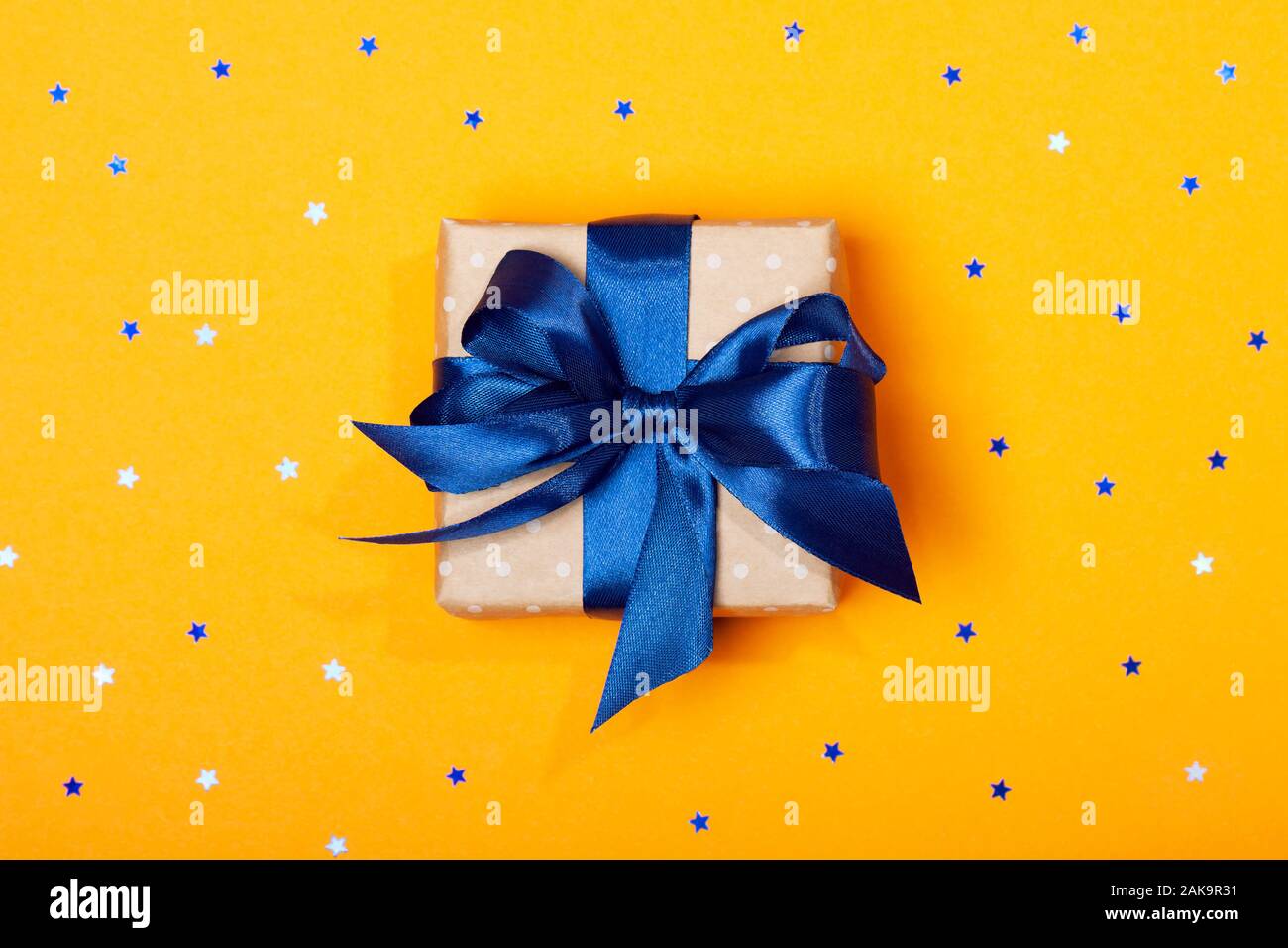 Attraente alla moda regalo con fiocco blu su sfondo arancione con le stelle. Buon Natale, il giorno di San Valentino, buon compleanno e gli altri giorni festivi concetto. Copia dello spazio. Foto Stock