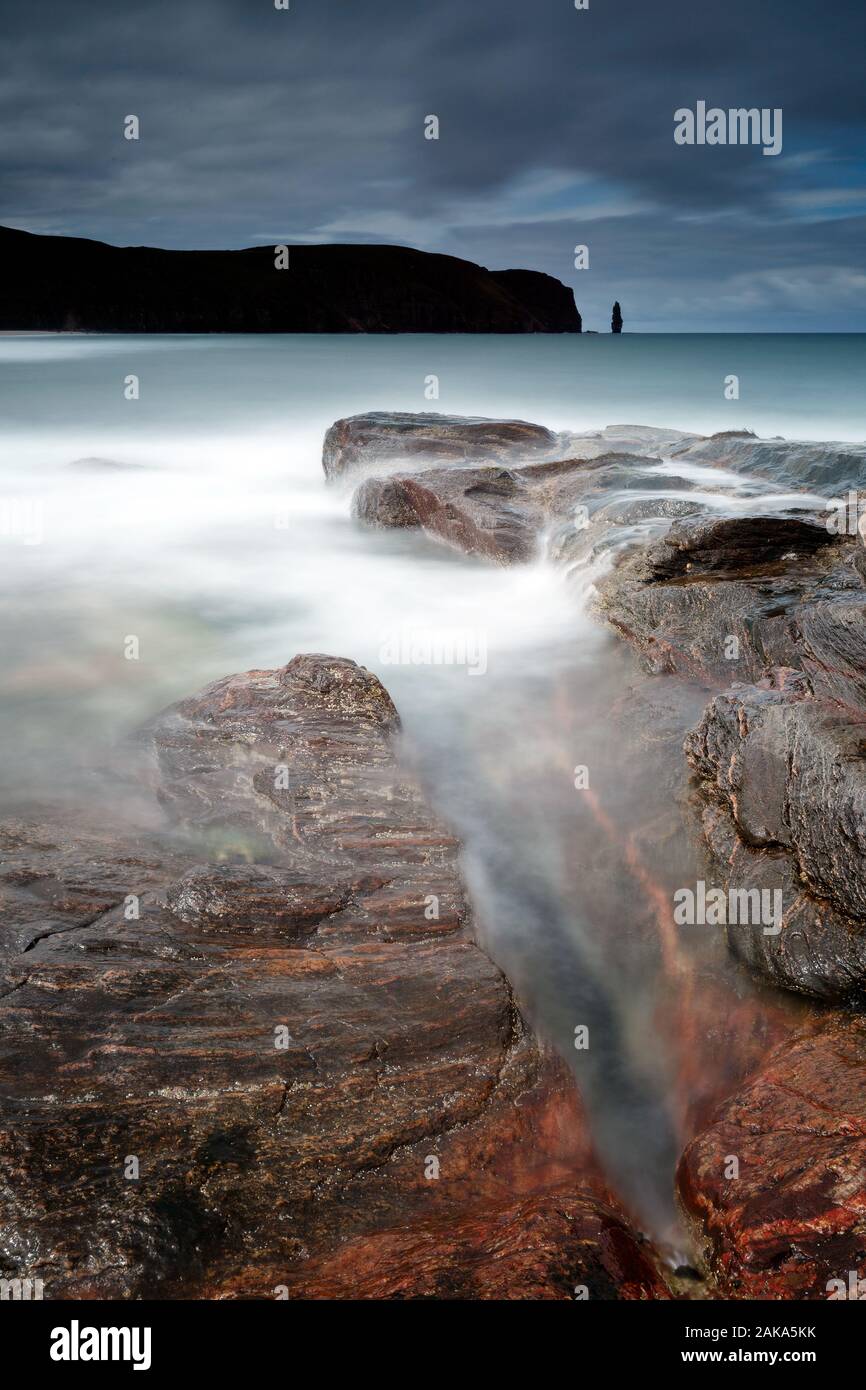 Sandwood Bay in Scozia con il Misty Waves a laminazione dal mare su scogli sulla riva con Am Buachaille stack di mare all'orizzonte Foto Stock