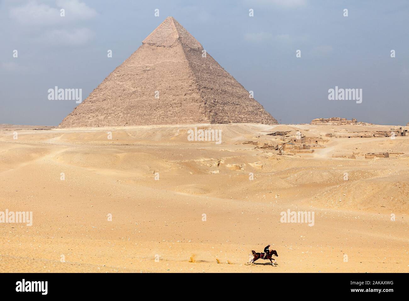 Un uomo corse a cavallo attraverso il deserto di sabbia su Giza altopiano presso le Grandi Piramidi d'Egitto Foto Stock