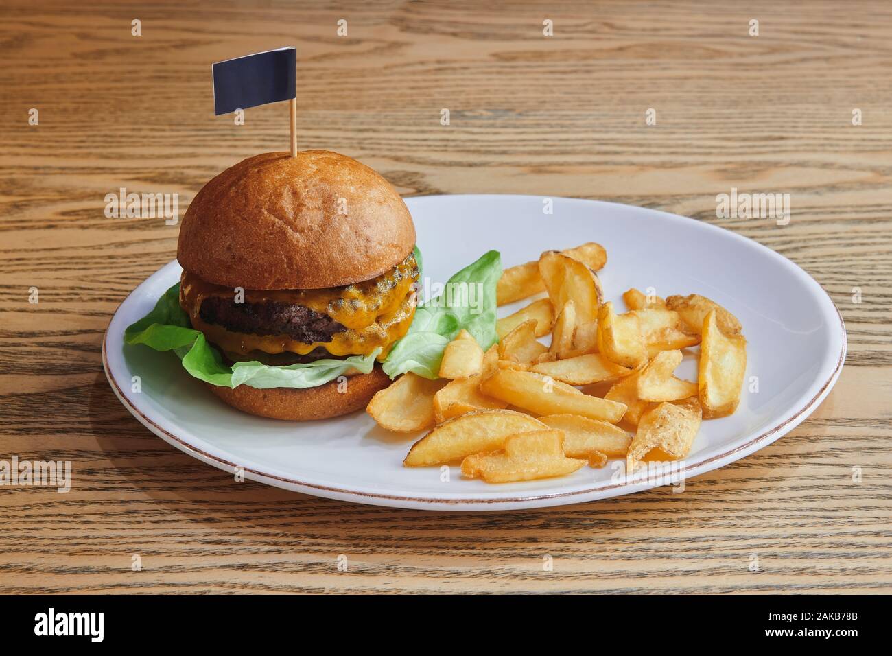 Doppio hamburger di manzo con doppio formaggio e insalata. Servito con i dippers di patate sul tavolo di legno nel piatto bianco. Cucina americana. Foto Stock