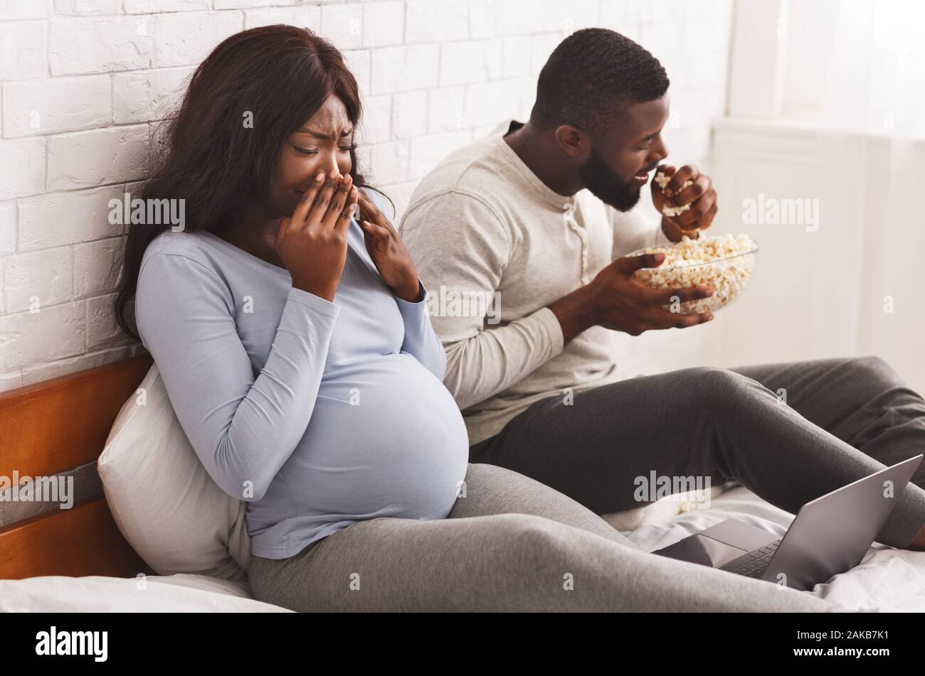 Olfatto durante la gravidanza. Afro uomo mangiare popcorn mentre la donna incinta allontana, arredamento Foto Stock