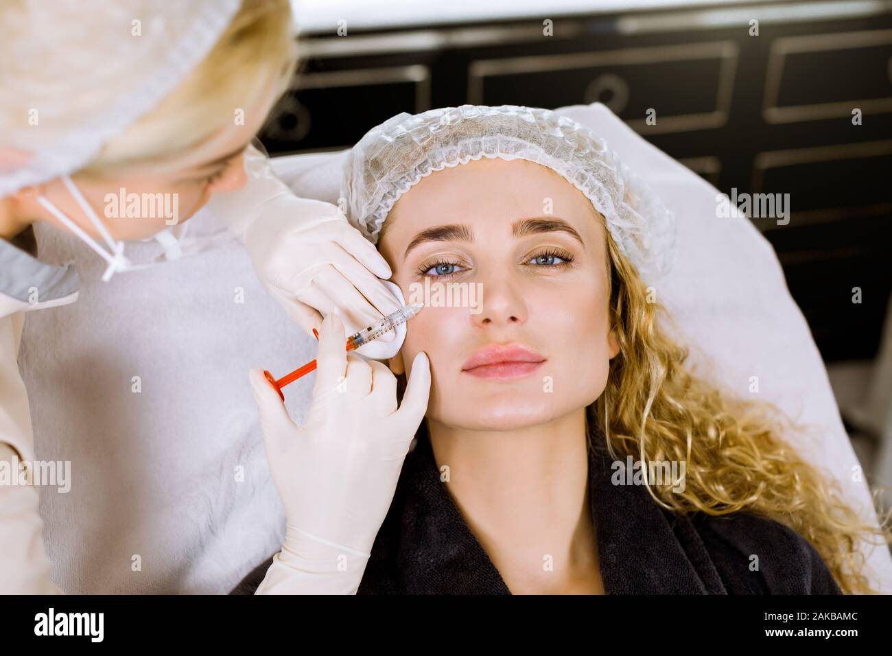 Il dottore cosmetologo rende il ringiovanimento di iniezioni per il viso la procedura di serraggio e levigatura di rughe sulla pelle del viso di una bella Foto Stock