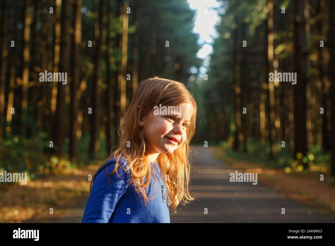Una bambina si trova in una foresta bagnata dalla luce dorata al tramonto Foto Stock