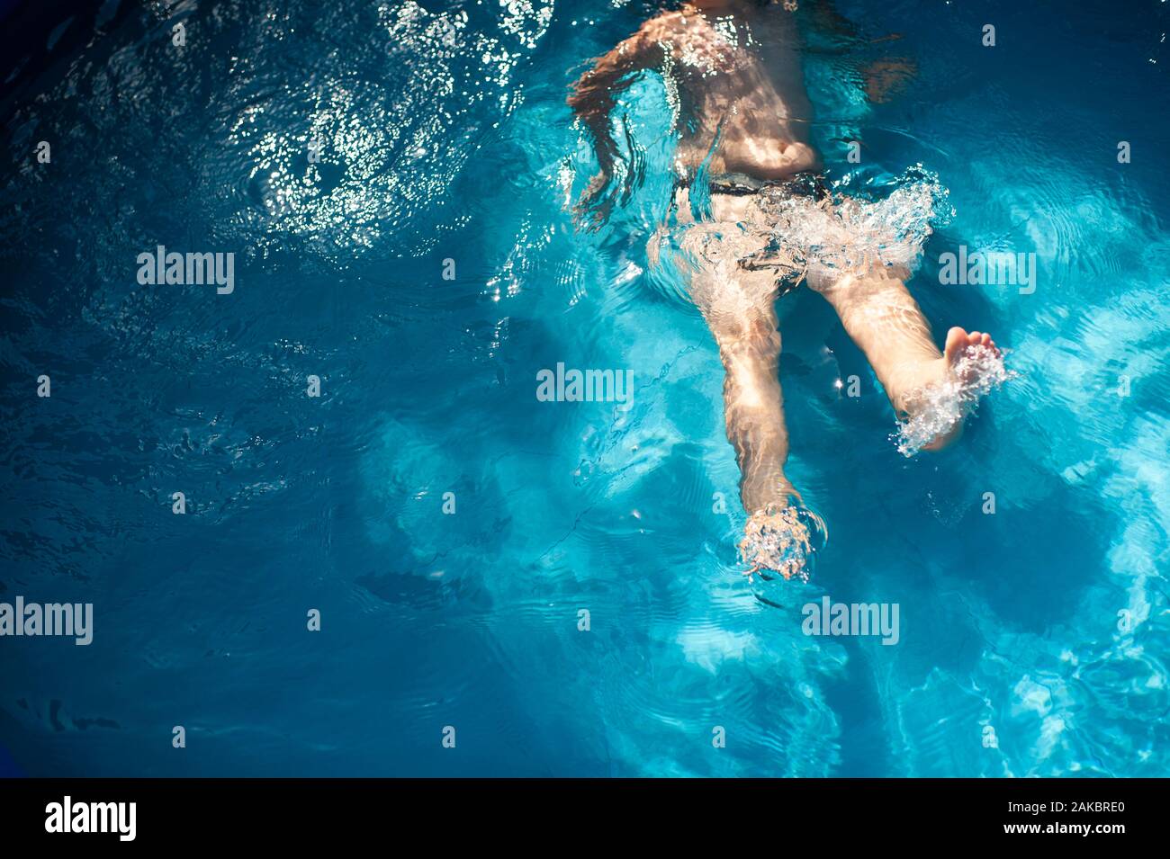 Il ragazzo di 7-8 anni si prende a calci in acqua in piscina durante l'estate Foto Stock
