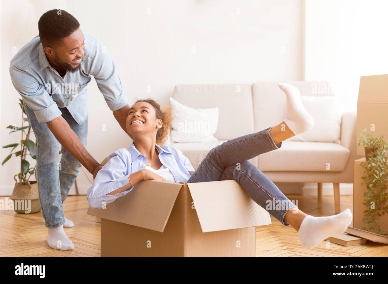 Spostando un nuovo appartamento. Gioiosa African American uomo Moglie di equitazione in una scatola di cartone interna dopo il trasferimento. Messa a fuoco selettiva Foto Stock