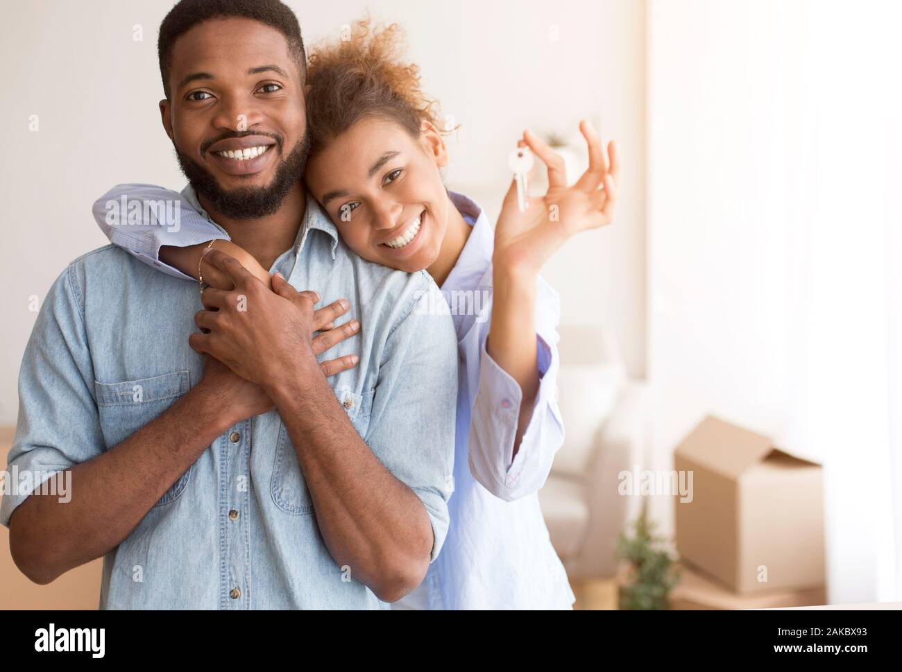 Concetto in movimento. Nero allegro giovane azienda Nuovo tasto Home abbracciando in piedi nella propria casa dopo il trasferimento. Il fuoco selettivo dello spazio libero Foto Stock