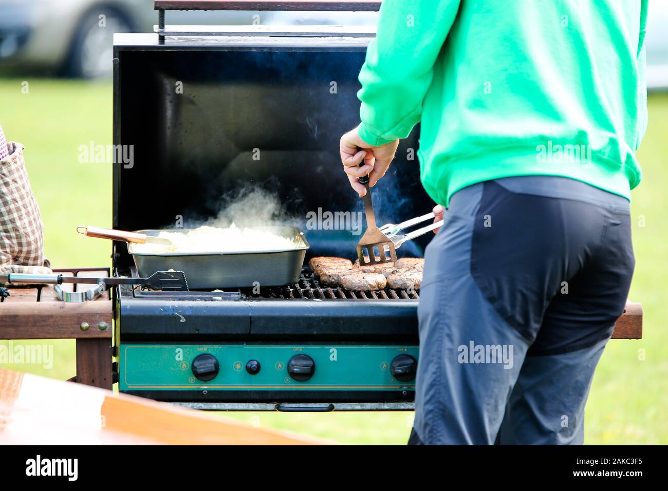 Un uomo la cottura di salsicce su un gas aperto barbeque, vi è anche un vassoio di cipolle in attesa di essere servito Foto Stock