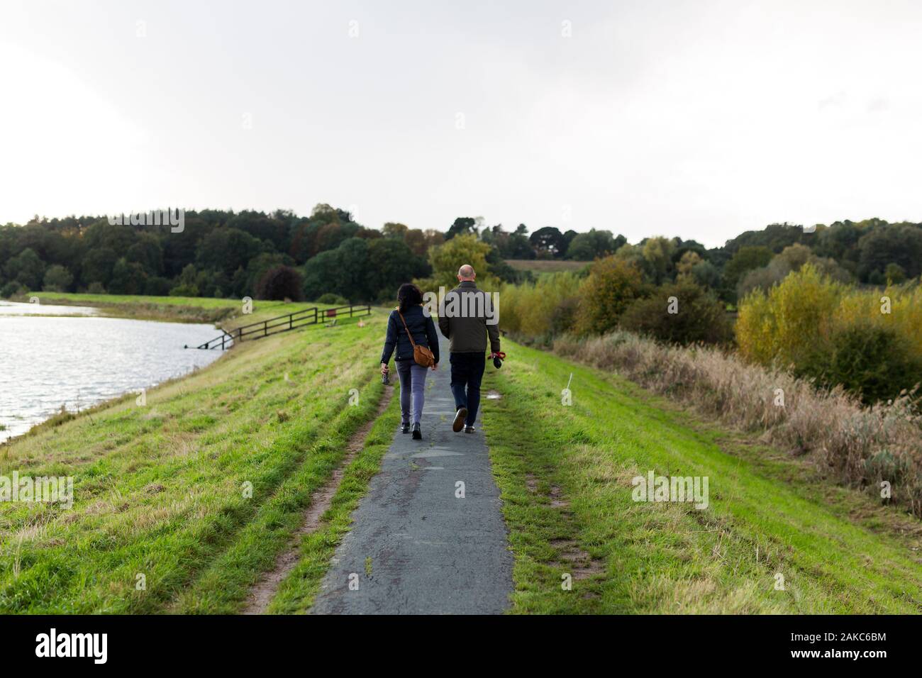 Una coppia di mezza età facendo una passeggiata lungo un fiume di percorso su un noioso pomeriggio autunnale Foto Stock