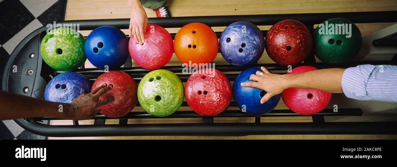 Tre popoli mani scegliendo le palle da bowling Foto Stock