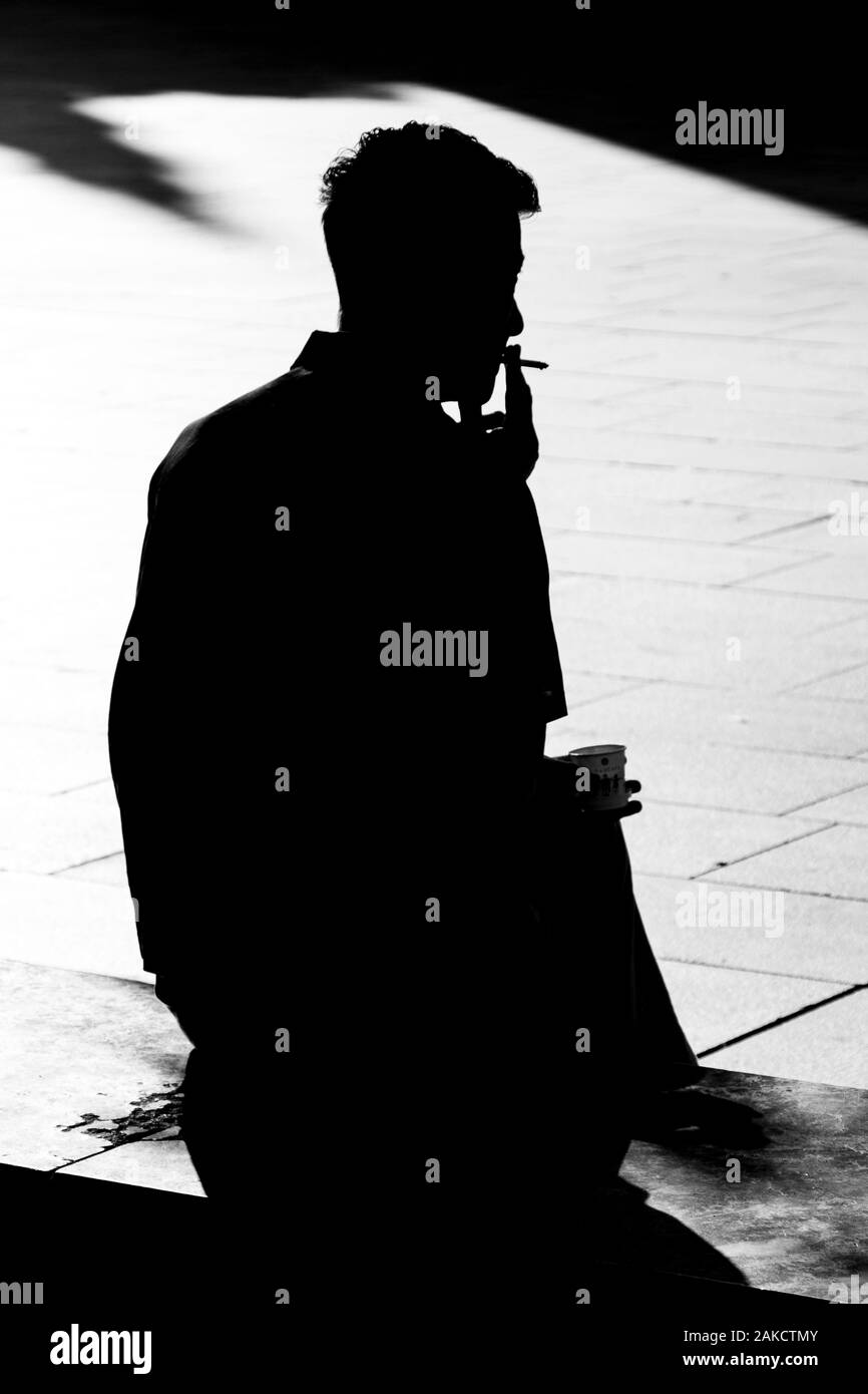 Silhouette di un uomo seduto mentre si fuma una sigaretta in Barcellona, Spagna. Foto Stock