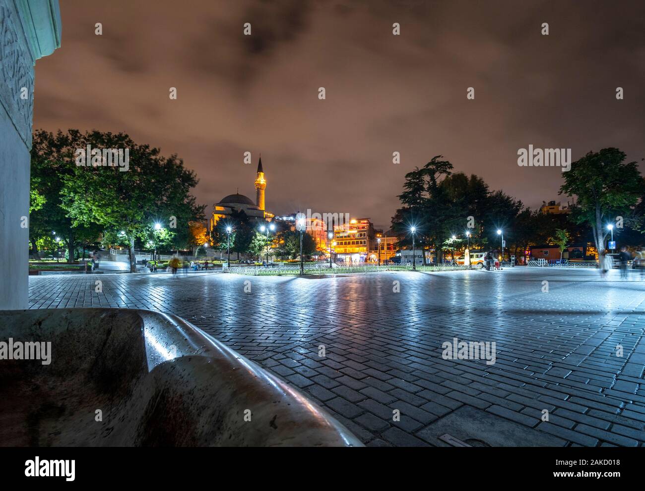 A tarda notte vista da Piazza Sultanahmet come turisti passano da vicino un minareto illuminato e moschea di Istanbul, Turchia Foto Stock
