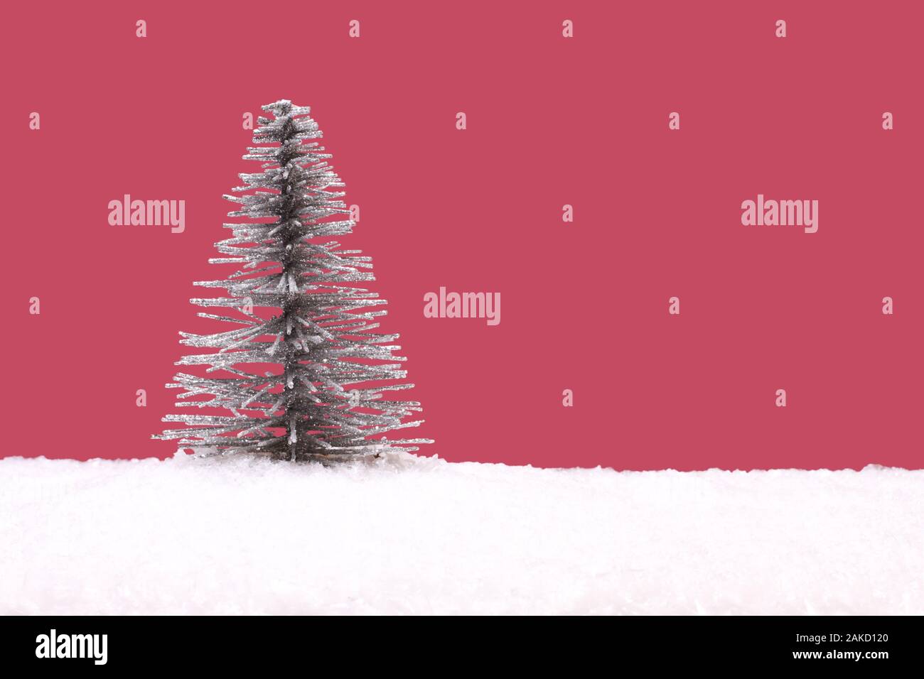 Toy argento albero di Natale artificiale sul bianco della neve contro sfondo rosa Foto Stock