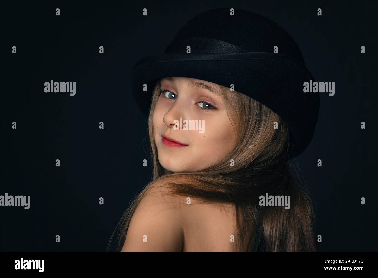 Bambina con un cappello nero e perle bianche.Ritratto di una bellissima bambina in stile retrò in un elegante cappello nero su sfondo nero.bambina. Foto Stock