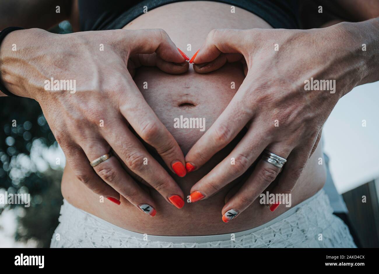 La donna incinta e il marito tenendo le sue mani a forma di cuore sul suo bambino bump Foto Stock