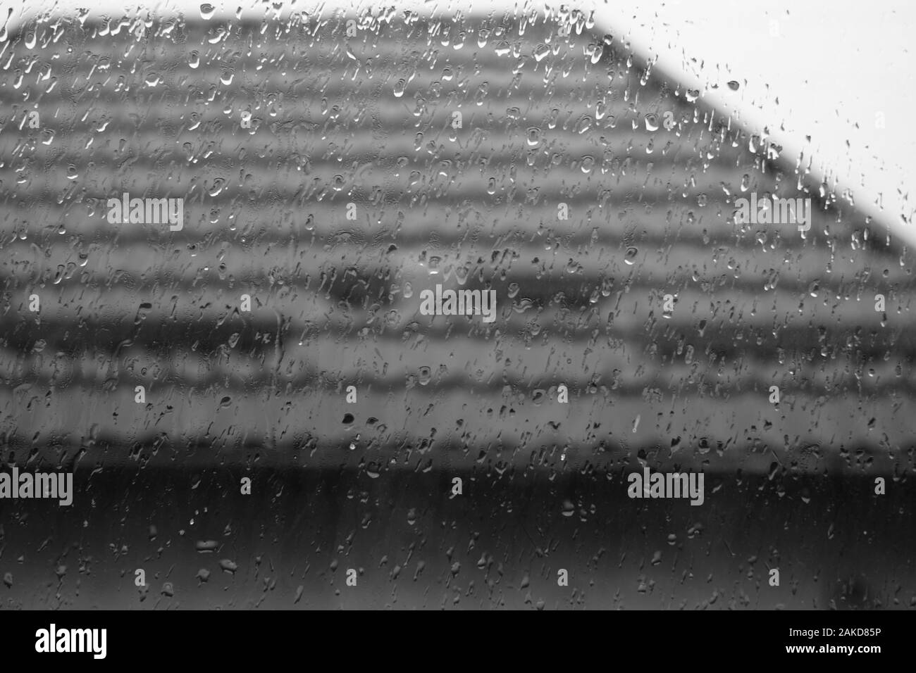 Finestra in gocce di pioggia, gocce d'acqua sul vetro, tetto di tegole per esterno Foto Stock