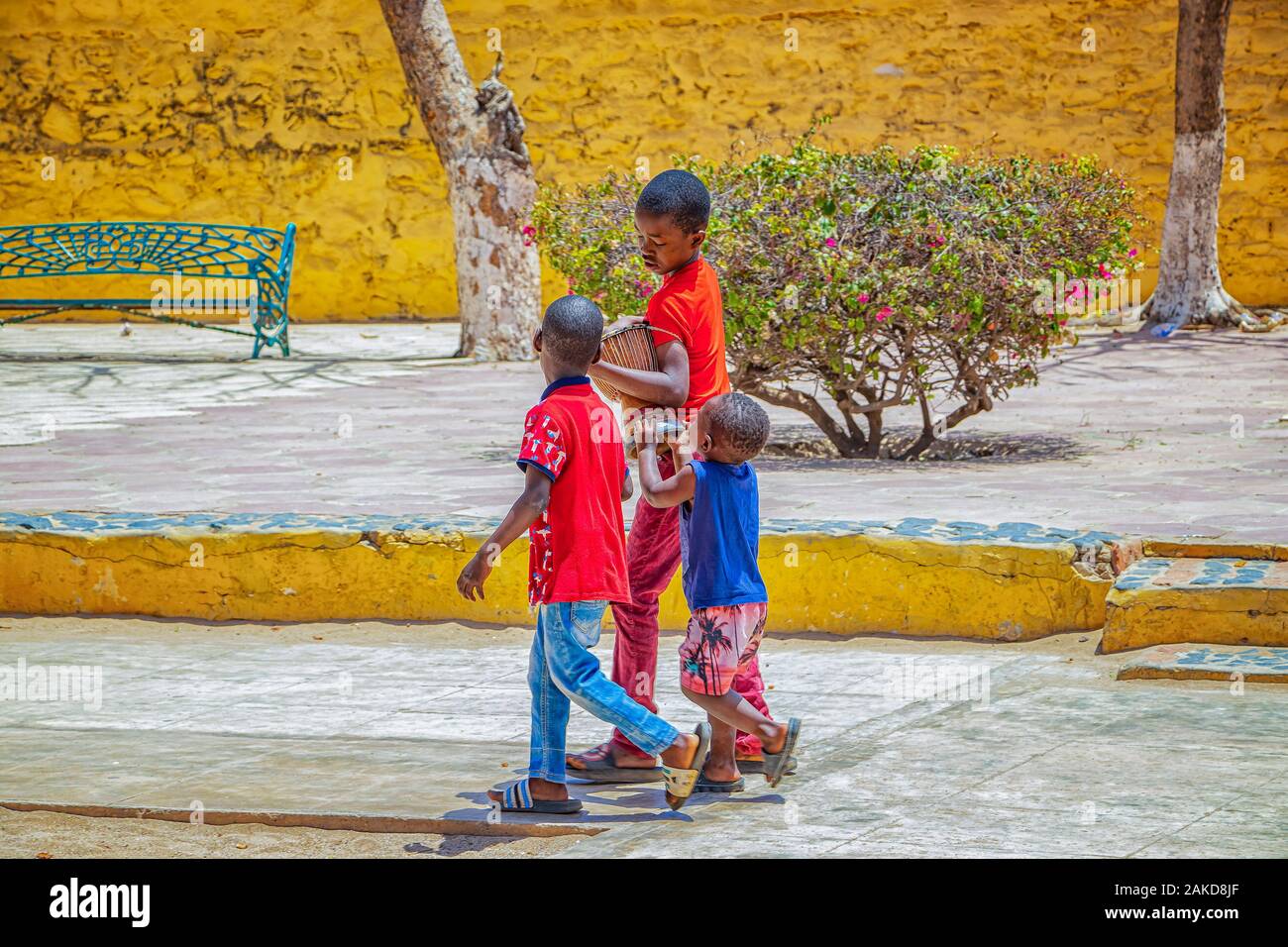 Isola di Goree, Senegal- 22 aprile 2019: ragazzi non identificato a piedi lungo una strada di sabbia in una piccola città e trasportare un tamburo di legno. Foto Stock