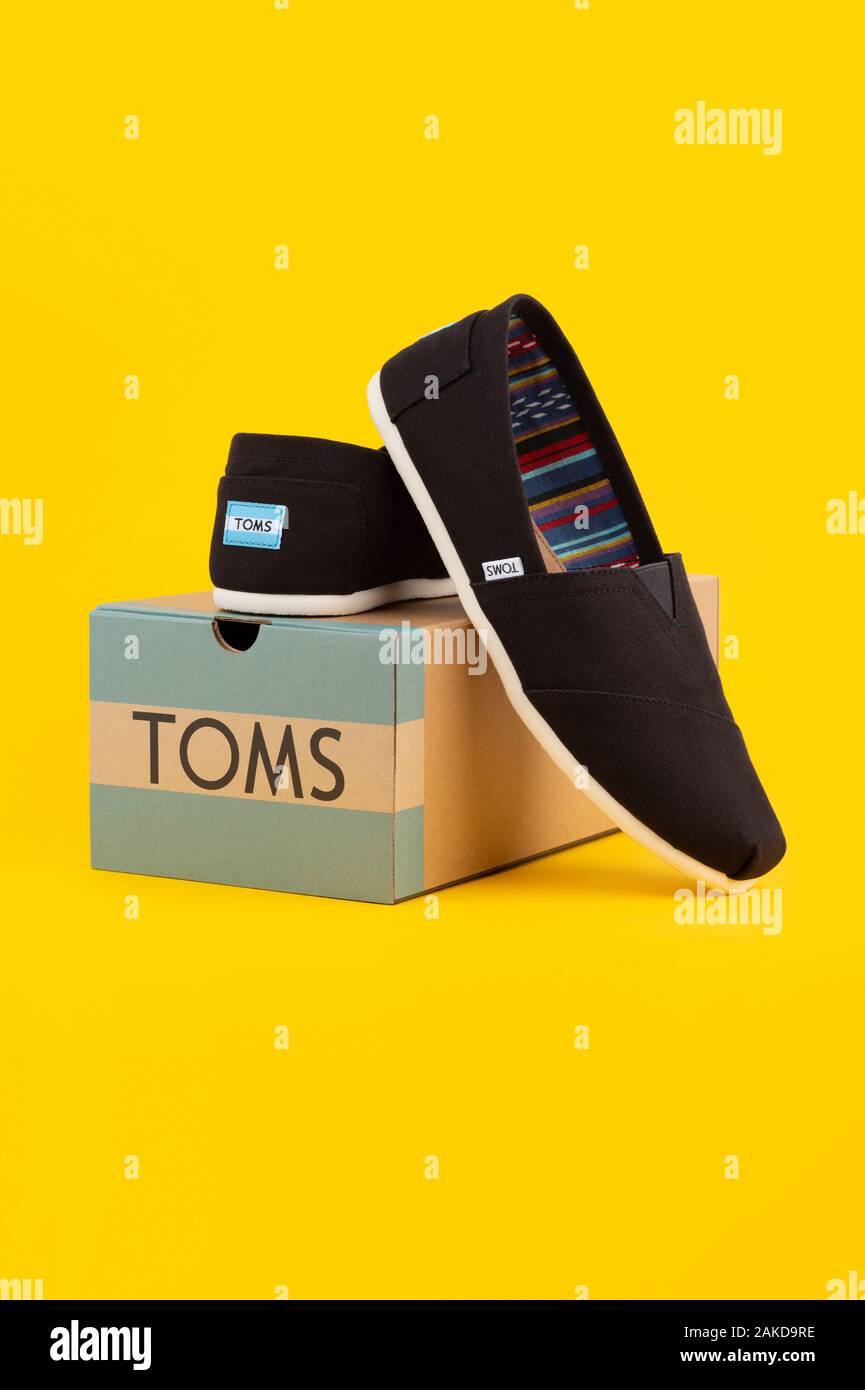 Una coppia di Toms Scarpe dalla società di raccolta di Venezia viene visualizzata da una scatola di scarpe di marca shot su sfondo giallo. Foto Stock
